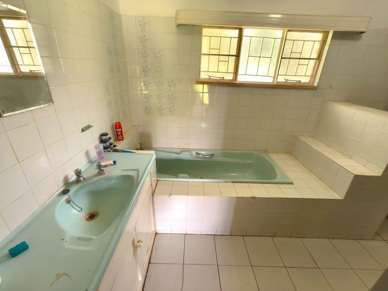 A dated bathroom featuring a built-in bathtub and vanity basin with original tiling, offering significant potential for a modern renovation.