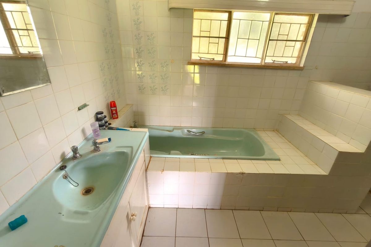 A dated bathroom featuring a built-in bathtub and vanity basin with original tiling, offering significant potential for a modern renovation.