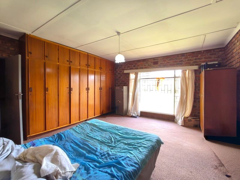 Spacious bedroom featuring extensive built-in wooden cupboards, an exposed brick feature wall, and large windows with security bars.