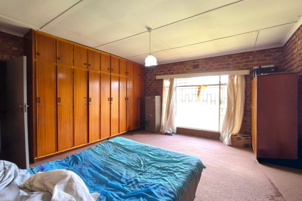 Spacious bedroom featuring extensive built-in wooden cupboards, an exposed brick feature wall, and large windows with security bars.
