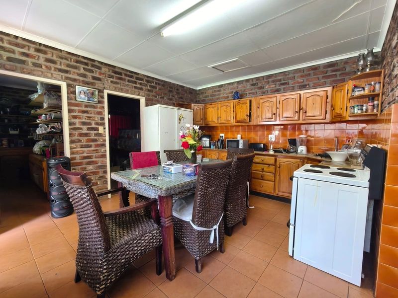 Open-plan kitchen and dining area featuring exposed brick walls, wooden cabinetry, and tiled flooring, offering a rustic and functional layout.