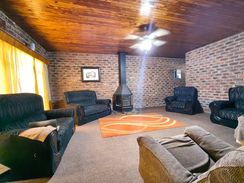 Spacious living room featuring rustic exposed brick walls, a warm timber ceiling, and a central freestanding fireplace.
