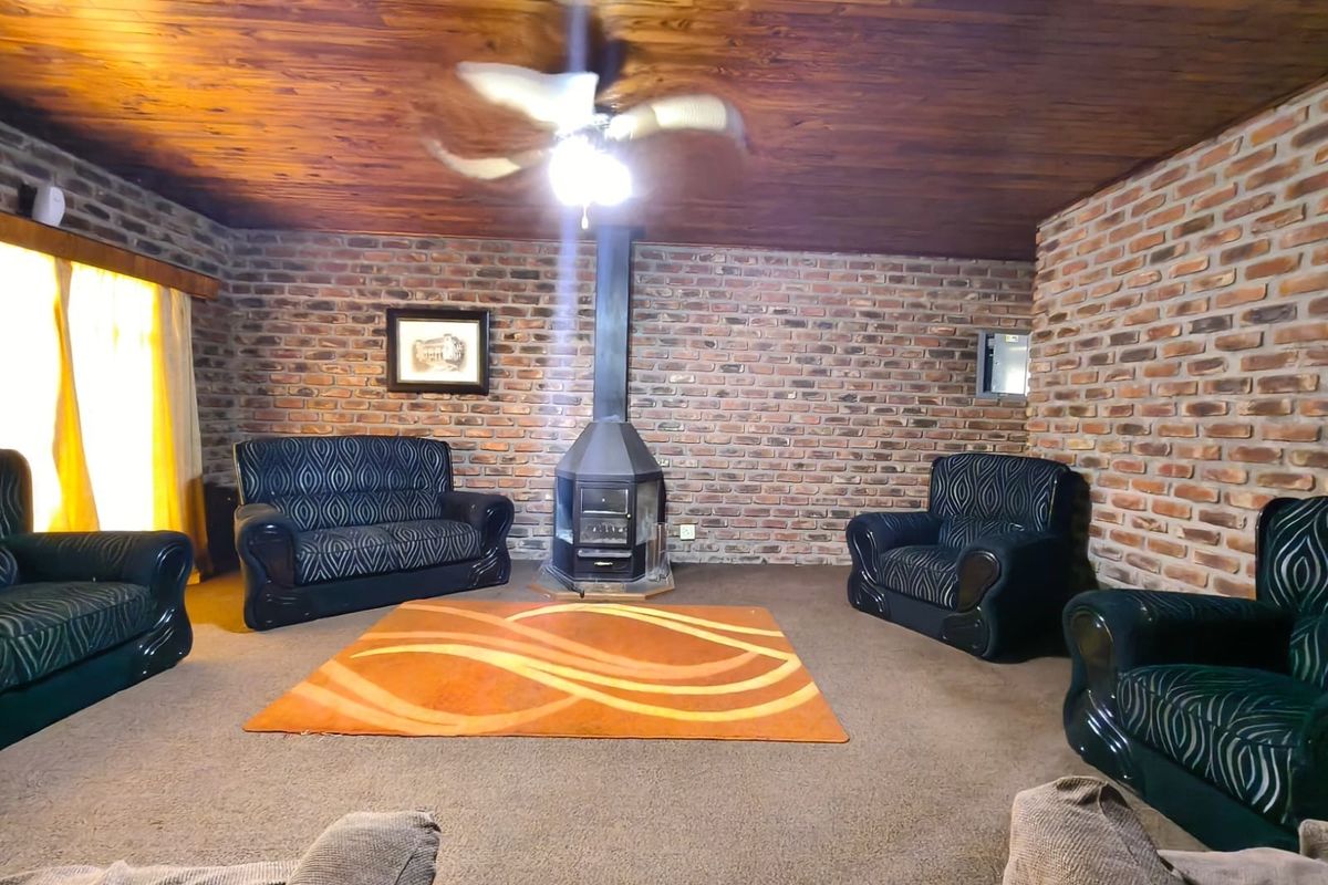 A rustic living room featuring exposed brick walls, a timber-clad ceiling, and a central freestanding fireplace.