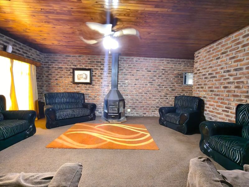 A rustic living room featuring exposed brick walls, a timber-clad ceiling, and a central freestanding fireplace.