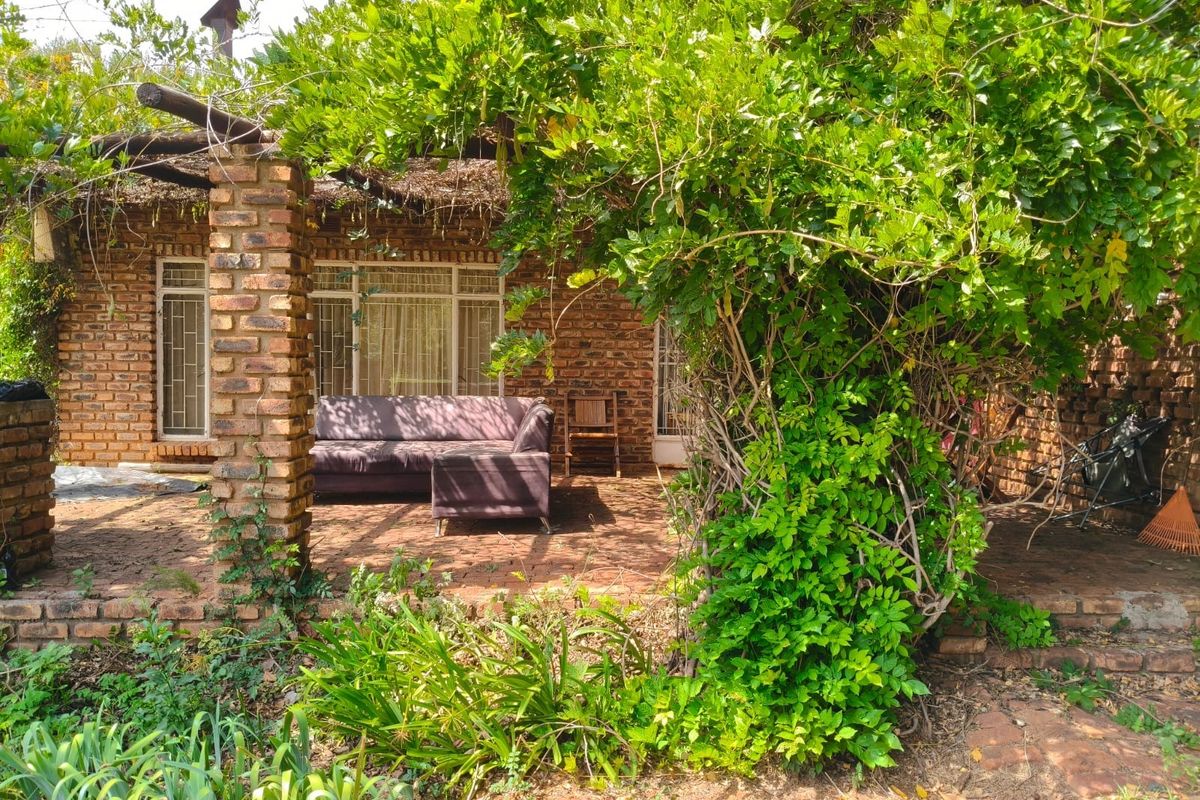 A rustic covered patio area featuring exposed brickwork, brick paving, and a timber pergola, surrounded by established garden greenery.