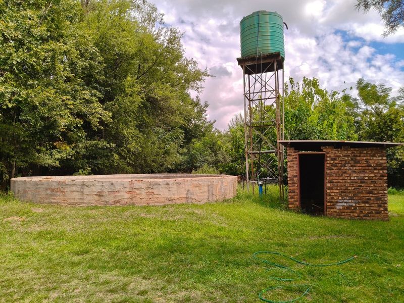 Outdoor area featuring a concrete reservoir, a raised water storage tank on a steel stand, and a small brick pump house structure.