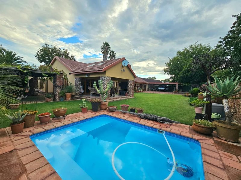 Spacious backyard featuring a swimming pool with brick coping, a well-maintained lawn, and a covered patio area attached to the main house.