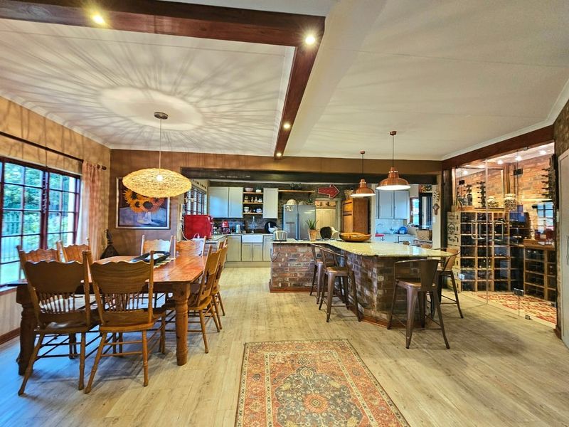 Spacious open-plan kitchen and dining area featuring exposed timber beams, a brick island with granite countertops, and a dedicated glass-enclosed wine cellar.