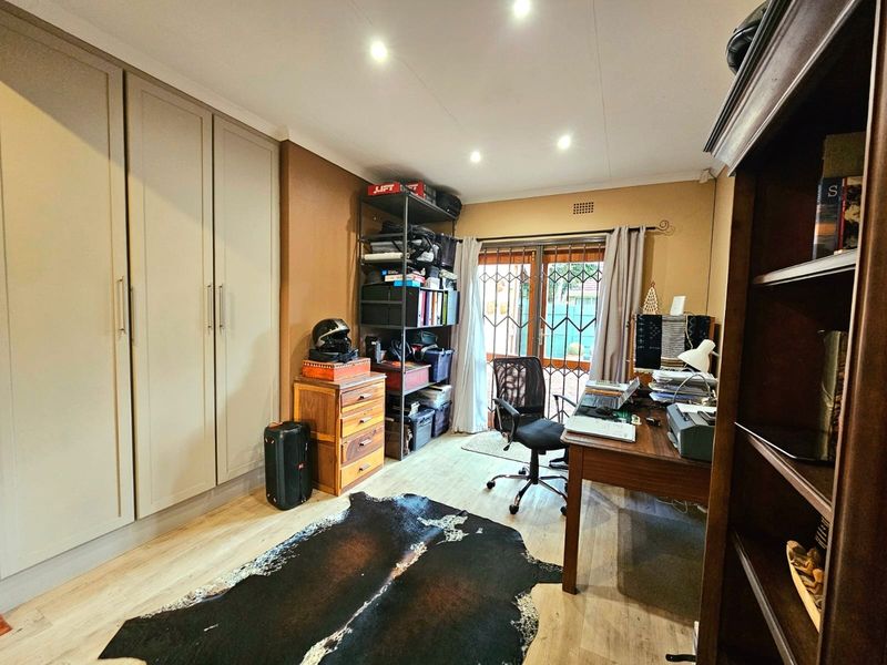 A functional home office featuring built-in cupboards, laminate flooring, and direct access to the garden through a sliding door with security gate.