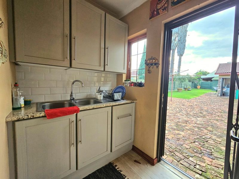 A functional scullery area featuring granite countertops, a double basin sink, subway tile backsplash, and direct access to the rear garden.
