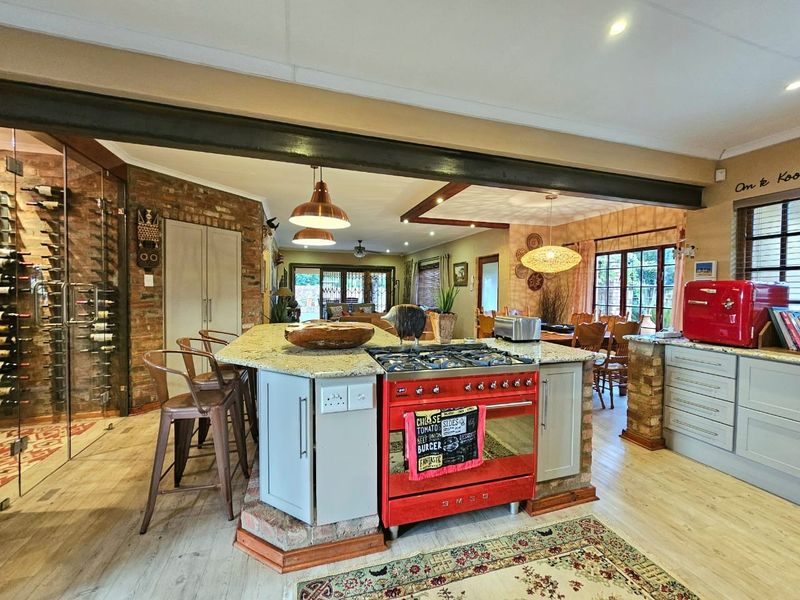 Spacious open-plan kitchen and living area featuring a central island with gas range, exposed brick accents, and a dedicated glass-enclosed wine storage unit.