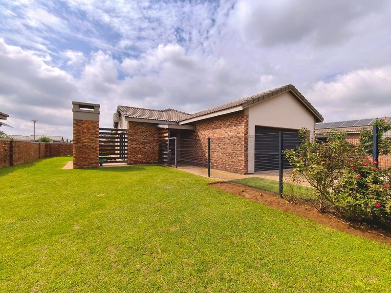 A well-maintained townhouse exterior featuring a face brick facade, tiled roof, and a private front garden with perimeter fencing and a paved driveway.