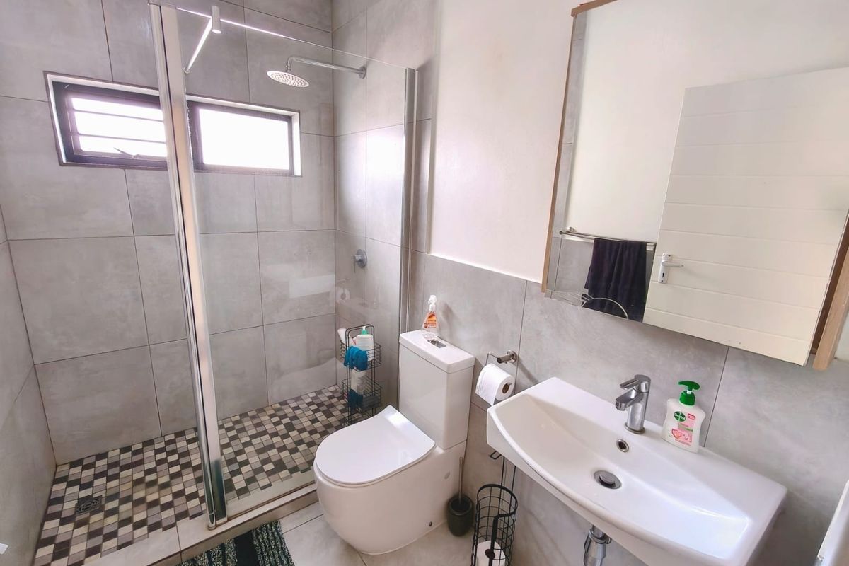 Modern bathroom featuring a walk-in shower with glass screen, wall-mounted basin, and contemporary grey tiling throughout.