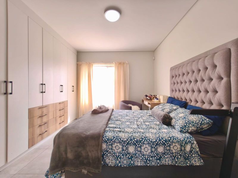 A well-maintained bedroom featuring extensive built-in cupboards with a modern two-tone finish and neutral tiled flooring.