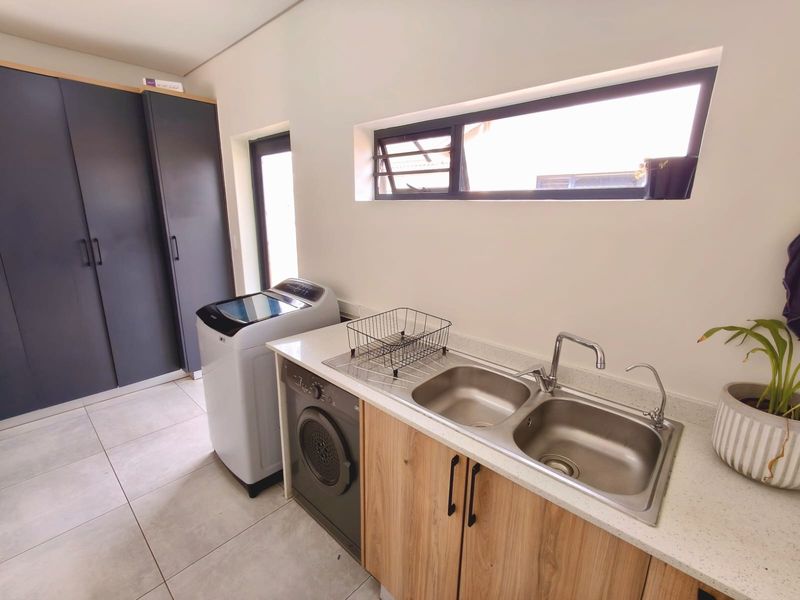 A functional laundry room featuring modern built-in cabinetry, a double stainless steel sink with stone countertops, and tiled flooring.