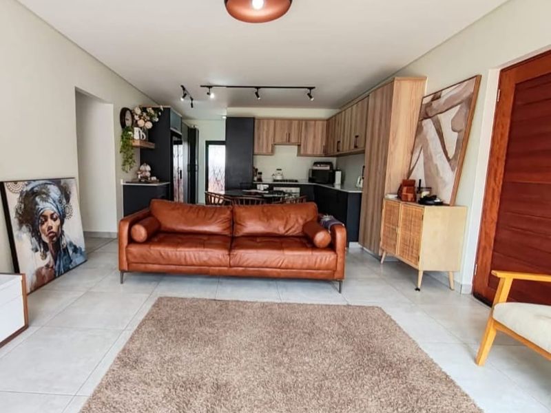 Modern open-plan living area featuring tiled floors, track lighting, and a contemporary kitchen with built-in cabinetry, seamlessly connecting to the main living space.