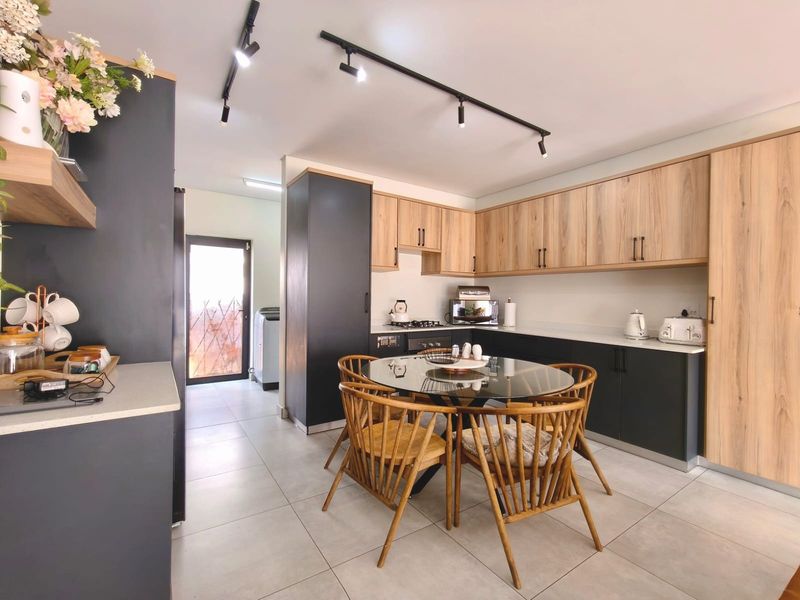 Modern open-plan kitchen and dining area featuring two-tone cabinetry, stone countertops, gas hob, built-in oven, and contemporary track lighting.