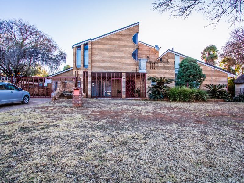 Front elevation of a multi-level brick house featuring a pitched roof, security gates, and a paved driveway.