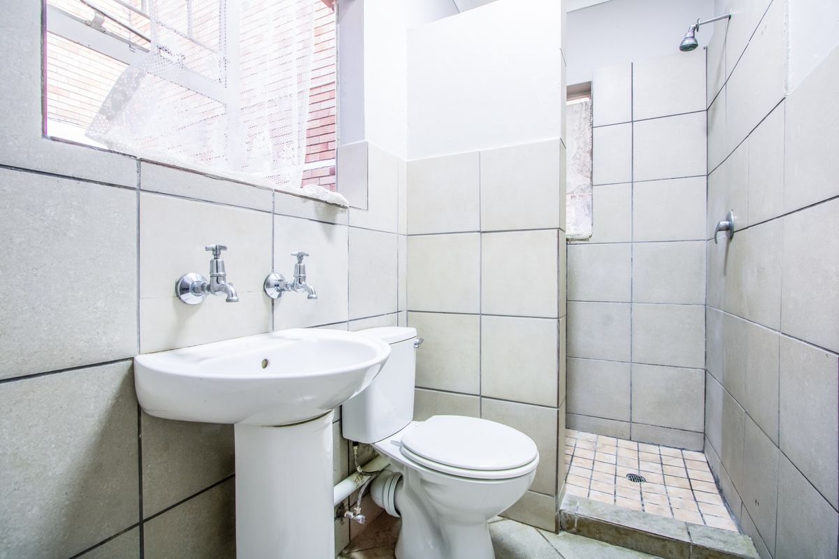 A functional bathroom featuring a pedestal basin, toilet, and a walk-in shower area with tiled finishes.