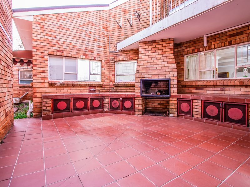 Covered outdoor patio area featuring a built-in braai, tiled flooring, and integrated brick cabinetry, providing a functional space for outdoor entertaining.