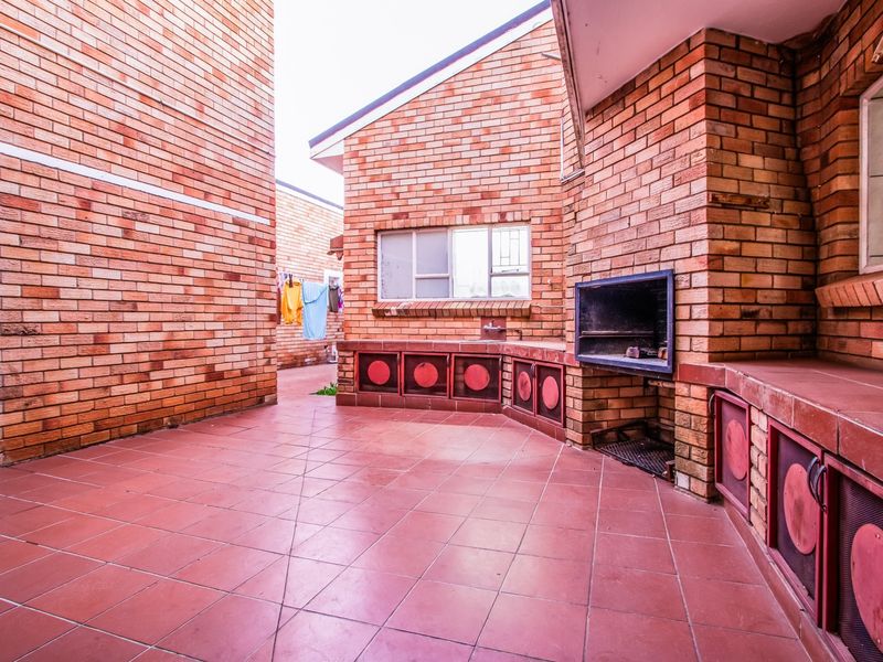 Covered outdoor patio area featuring face-brick walls, tiled flooring, and a built-in braai facility with an integrated sink.