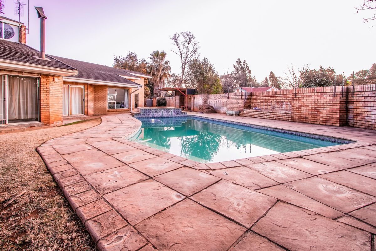Outdoor pool area featuring a paved deck, brick boundary wall, and a swimming pool with a raised water feature.