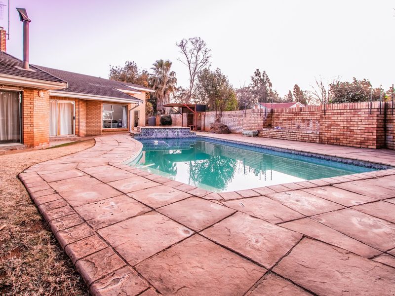 Outdoor pool area featuring a paved deck, brick boundary wall, and a swimming pool with a raised water feature.