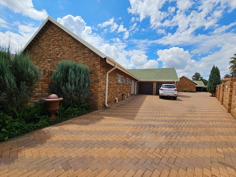 A well-maintained townhouse exterior featuring a face brick facade, a spacious paved driveway, and a double garage with a tiled roof.