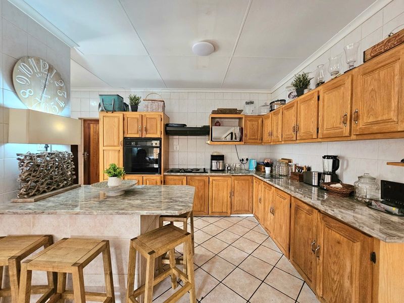 A functional kitchen featuring traditional wooden cabinetry, stone countertops, a built-in oven, gas hob, and a convenient breakfast nook with tiled flooring.