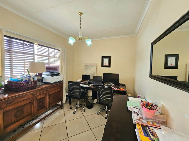 A functional home office space featuring tiled flooring, venetian blinds, and a classic pendant light fixture, providing a practical area for work or study.