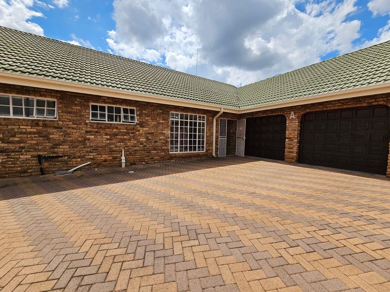 Front exterior view of a townhouse featuring a brick facade, tiled roof, paved driveway, and double garage access.