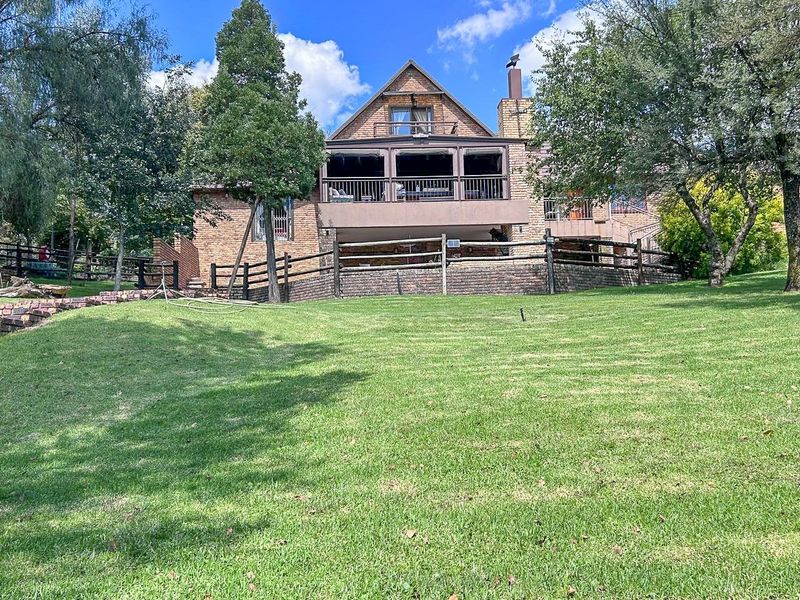 Rear view of a multi-story brick house featuring a spacious covered balcony, chimney, and a large landscaped garden with timber fencing.