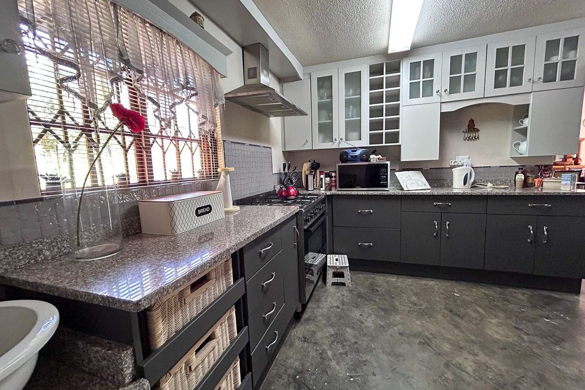 A functional kitchen featuring dark grey cabinetry, granite countertops, a gas stove with extractor fan, and ample storage with glass-fronted upper cabinets.