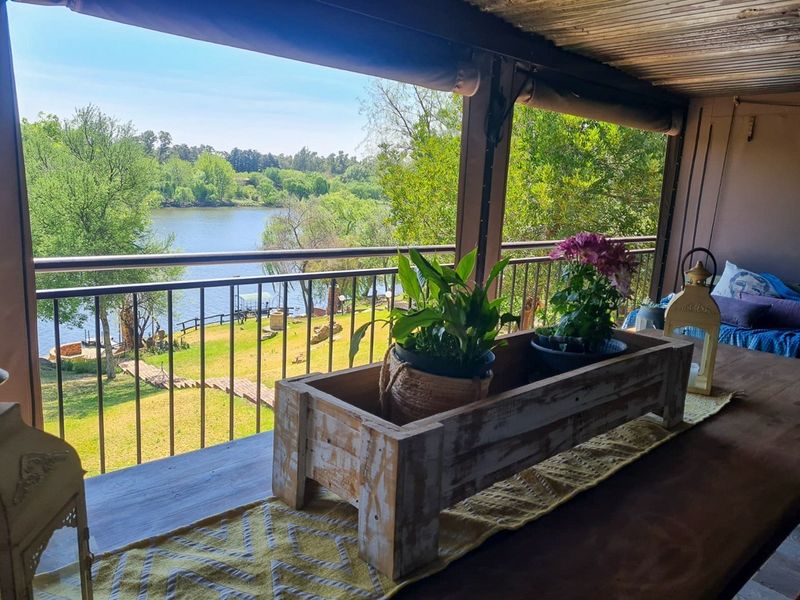 Covered balcony featuring a metal railing and timber ceiling, offering scenic views of the river and surrounding garden.