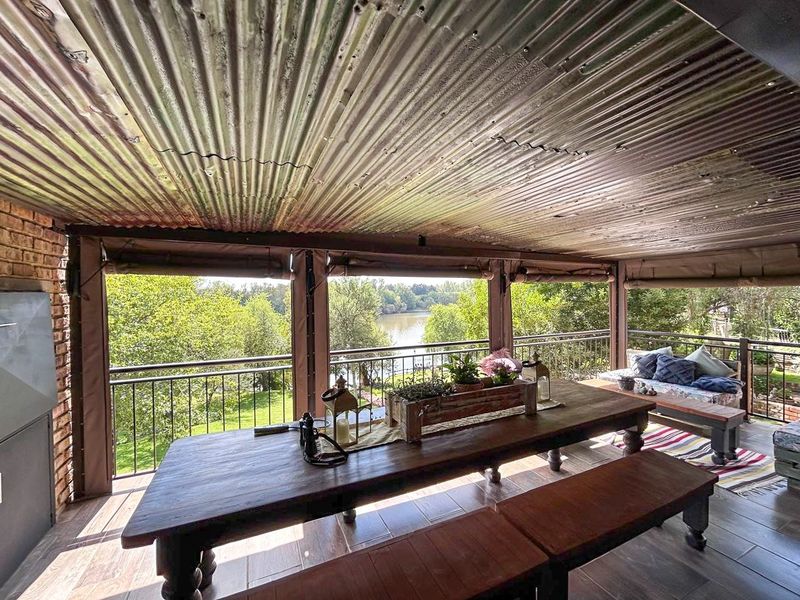 Covered outdoor patio featuring a corrugated metal roof, tiled flooring, and metal railings, offering scenic views of the surrounding greenery and water.