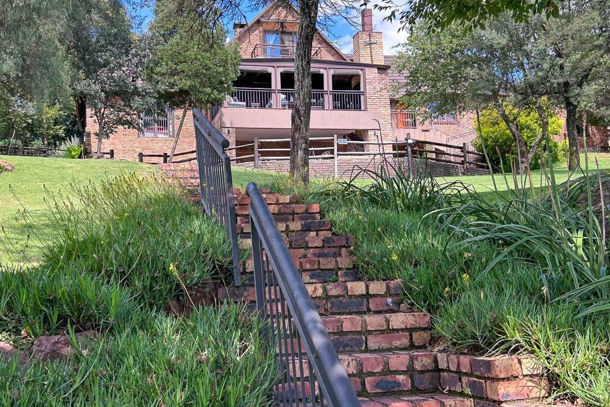 Rear view of a multi-story brick house featuring a covered balcony, chimney, and a brick staircase leading through the landscaped garden.