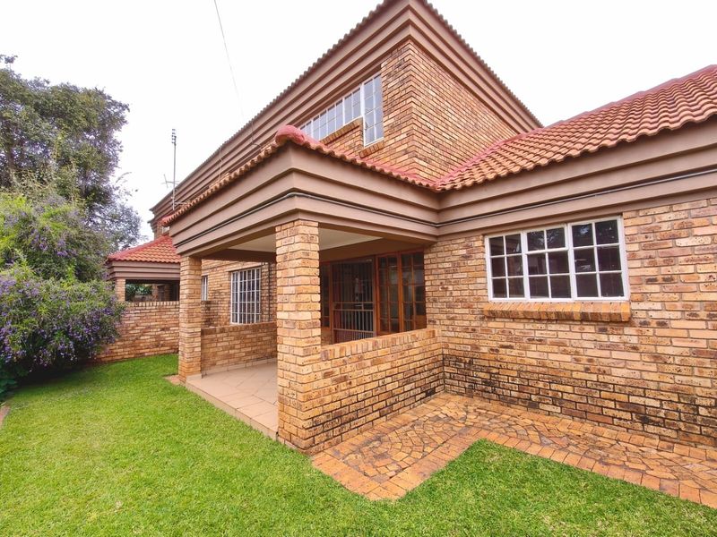 Rear view of a face brick townhouse featuring a covered patio, tiled roof, and well-maintained garden area with brick paving.