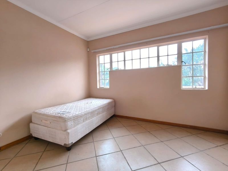 A spacious, empty bedroom featuring neutral tiled flooring, large multi-pane windows, and coved ceilings, offering a blank canvas for personalization.