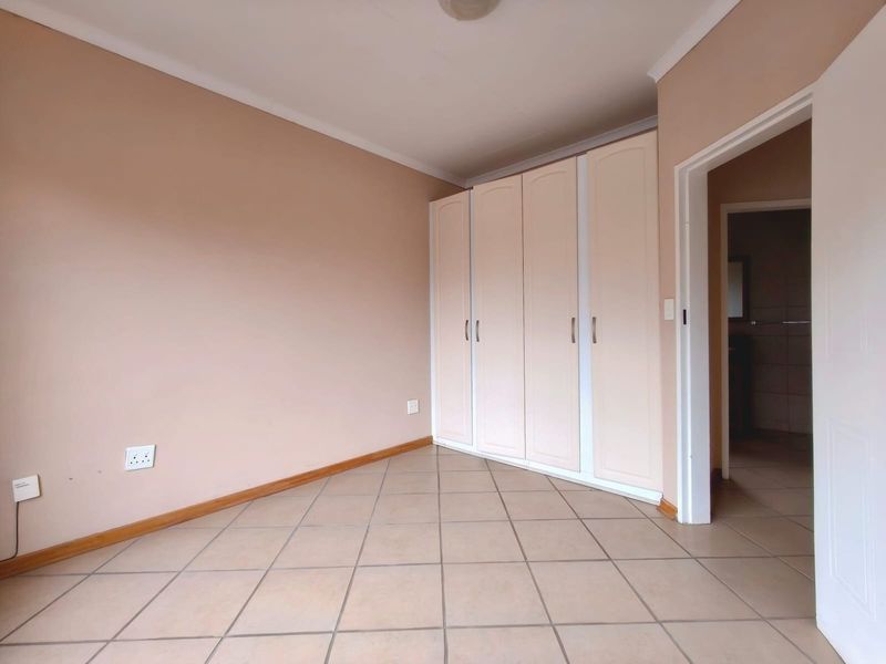 A clean, empty bedroom featuring neutral wall tones, tiled flooring, and a functional built-in wardrobe with access to an adjoining room.