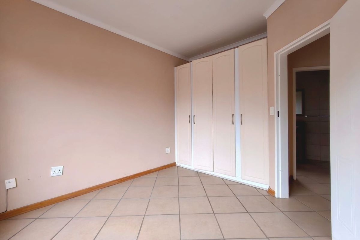 A clean, empty bedroom featuring neutral wall tones, tiled flooring, and a functional built-in wardrobe with access to an adjoining room.