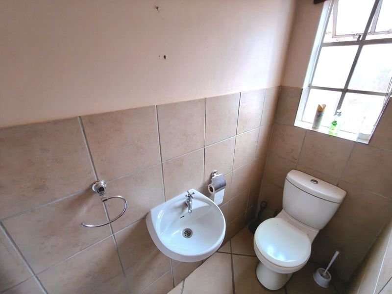 A compact guest bathroom featuring a wall-mounted basin, toilet, and neutral tiled finishes, offering a functional space ready for cosmetic updates.