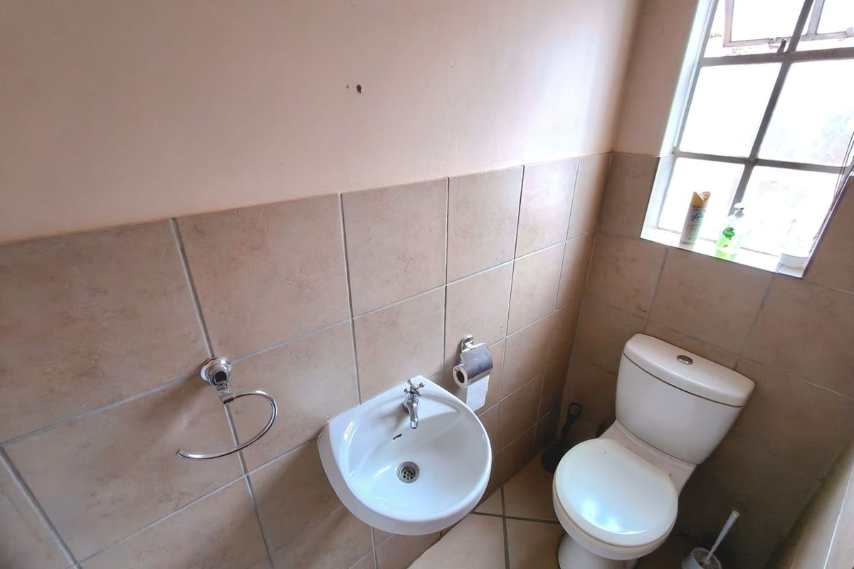 A compact guest bathroom featuring a wall-mounted basin, toilet, and neutral tiled finishes, offering a functional space ready for cosmetic updates.