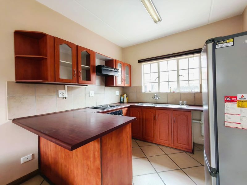 A functional kitchen featuring wooden cabinetry, laminate countertops, a built-in hob and oven, and tiled flooring with a window for natural light.