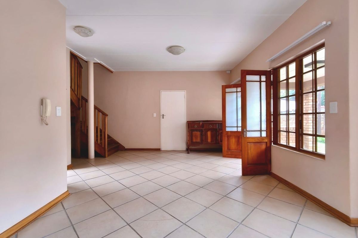 Spacious living area featuring neutral tiled flooring, a wooden staircase, and large windows providing natural light, offering a versatile open-plan layout.