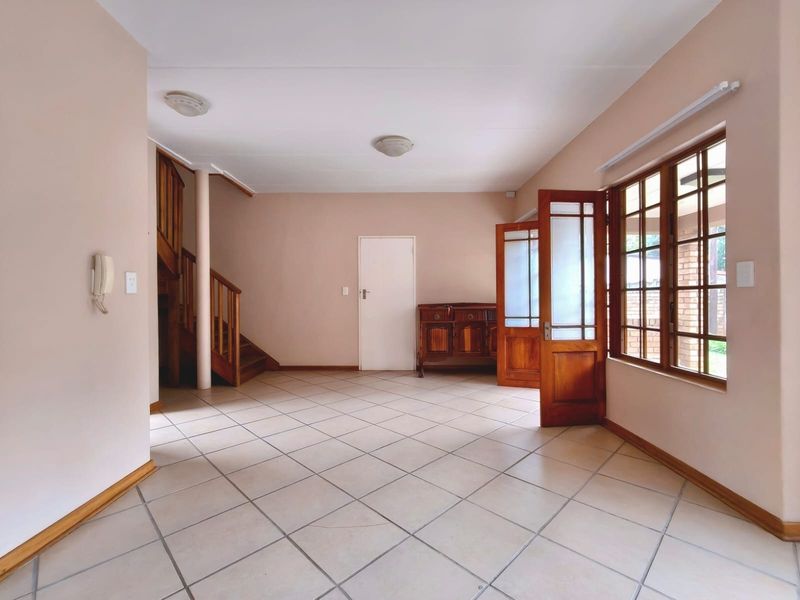 Spacious living area featuring neutral tiled flooring, a wooden staircase, and large windows providing natural light, offering a versatile open-plan layout.