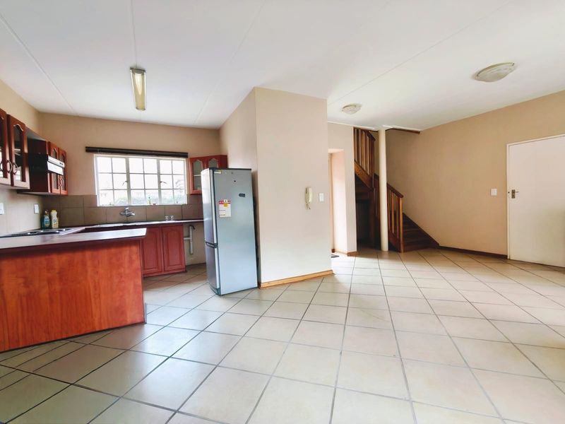 Open-plan kitchen and living area featuring tiled floors, wooden cabinetry, and a staircase leading to the upper level.