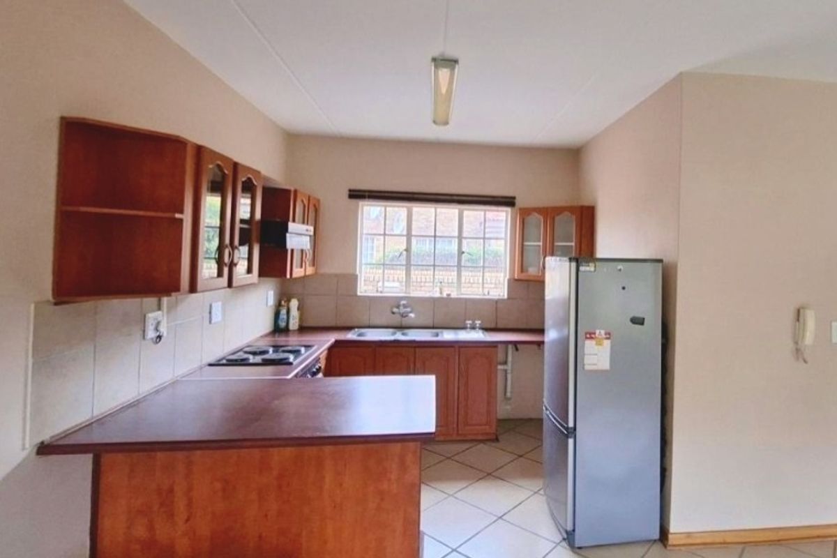 A functional kitchen featuring wooden cabinetry, laminate countertops, a built-in hob with extractor fan, and tiled flooring with a neutral backsplash.