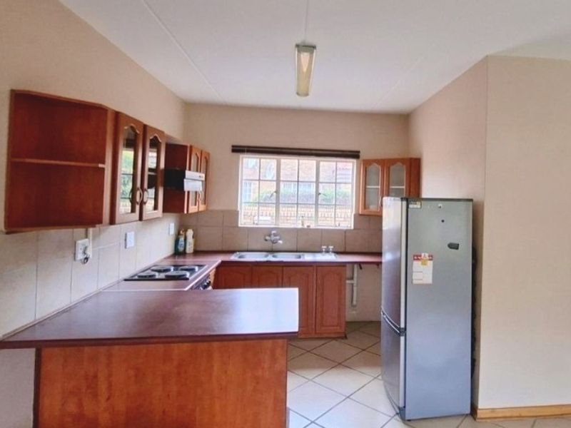 A functional kitchen featuring wooden cabinetry, laminate countertops, a built-in hob with extractor fan, and tiled flooring with a neutral backsplash.