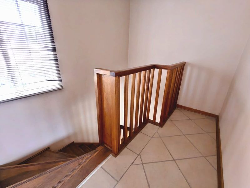 A bright landing area featuring a wooden staircase with a matching balustrade and neutral tiled flooring.