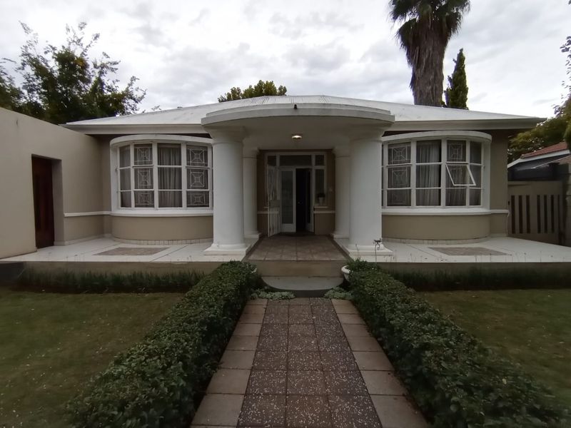 Front elevation of a charming house featuring a covered porch with classical columns, symmetrical bay windows, and a well-maintained hedged garden path.